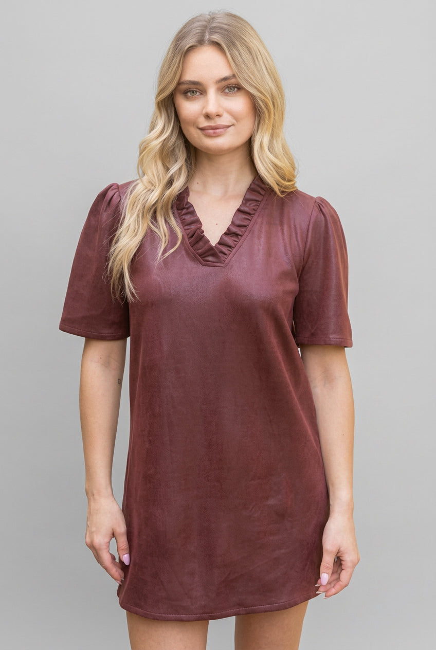 A woman modeling a short-sleeve, v-neck with ruffle dress in a burgundy faux leather fabric, set against a gray background