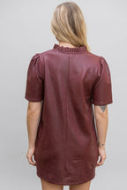 Back view of a woman modeling a short-sleeve, v-neck with ruffle dress in a burgundy faux leather fabric, set against a gray background