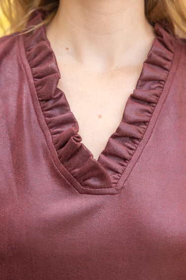 Close-up of a person wearing a burgundy faux leather dress with a ruffled V-neck trim.