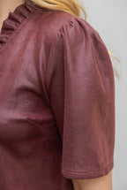 Close-up of a person wearing a short-sleeve dress in burgundy faux leather, showing the shoulder, sleeve, and part of the neckline against a gray background