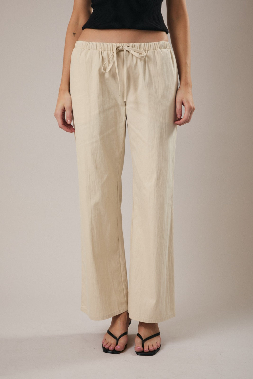 Woman wearing straight leg ecru drawstring pants against a grey background