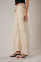 Woman wearing straight leg ecru drawstring pants against a grey background