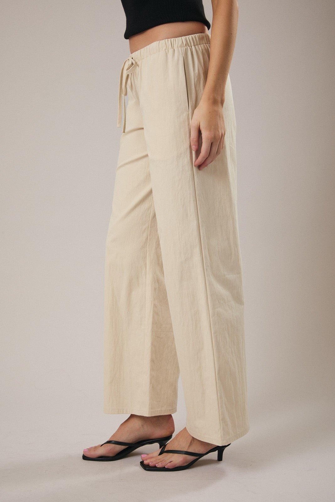 Woman wearing straight leg ecru drawstring pants against a grey background