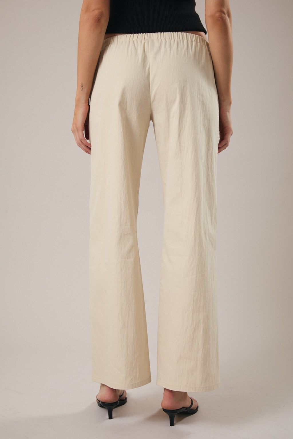 Back view of a woman wearing straight leg ecru drawstring pants against a grey background