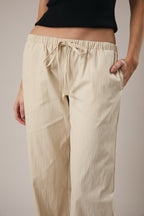 Woman wearing straight leg ecru drawstring pants against a grey background