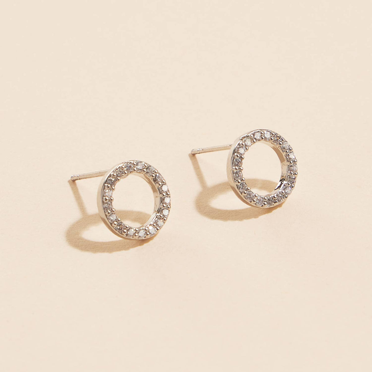 Open circle pave cubic zirconia stud earrings on a beige background