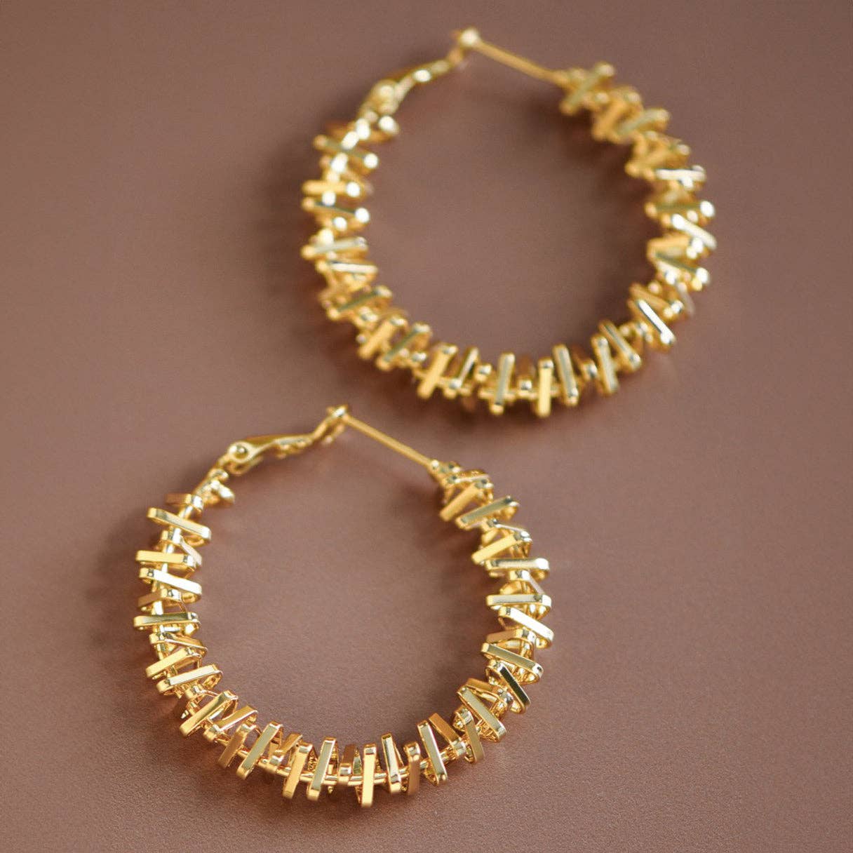 Gold tone textured hoop earrings on a brown background