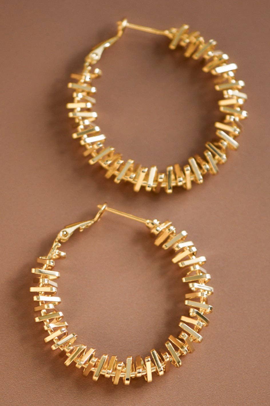 Gold two tone textured hoop earrings on a brown background