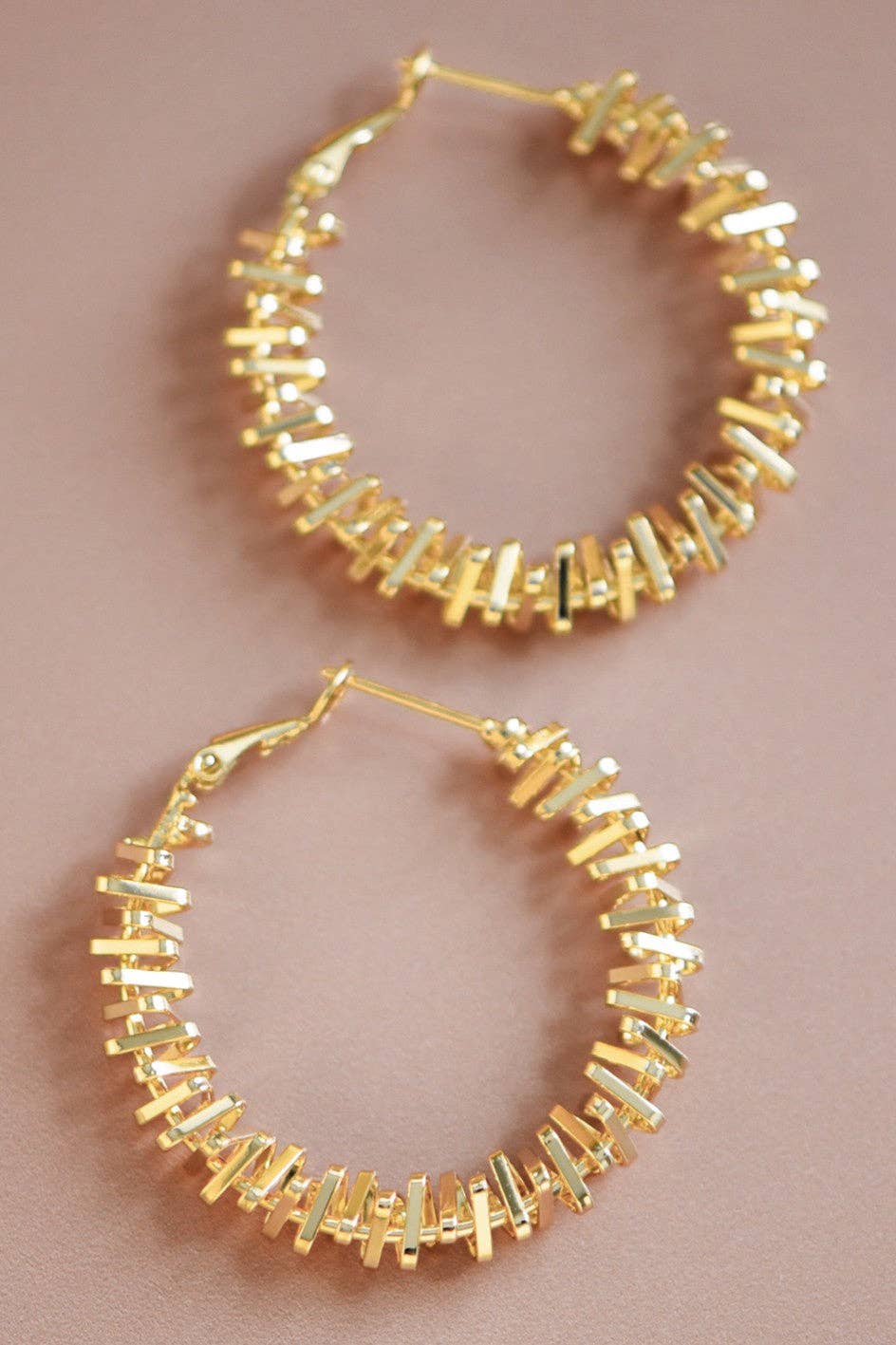 Gold tone textured hoop earrings on a pink background