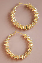 Gold tone textured hoop earrings on a pink background