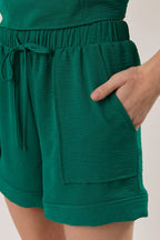 Woman wearing hunter green shorts with patch pockets against a white background
