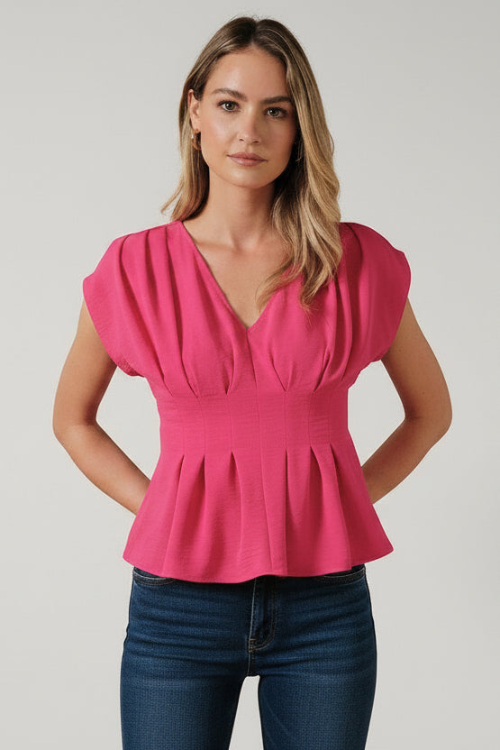 Woman wearing a fuchsia pleated peplum top and blue jeans against a beige background