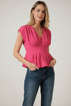 Woman wearing a fuchsia pleated peplum top and blue jeans against a beige background