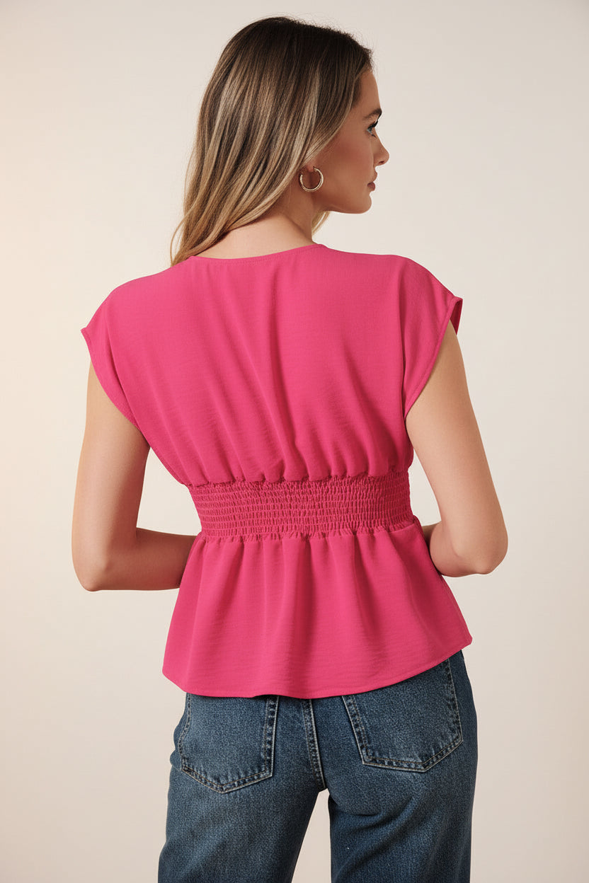 Back view of a woman wearing a fuchsia pleated peplum top and blue jeans against a beige background