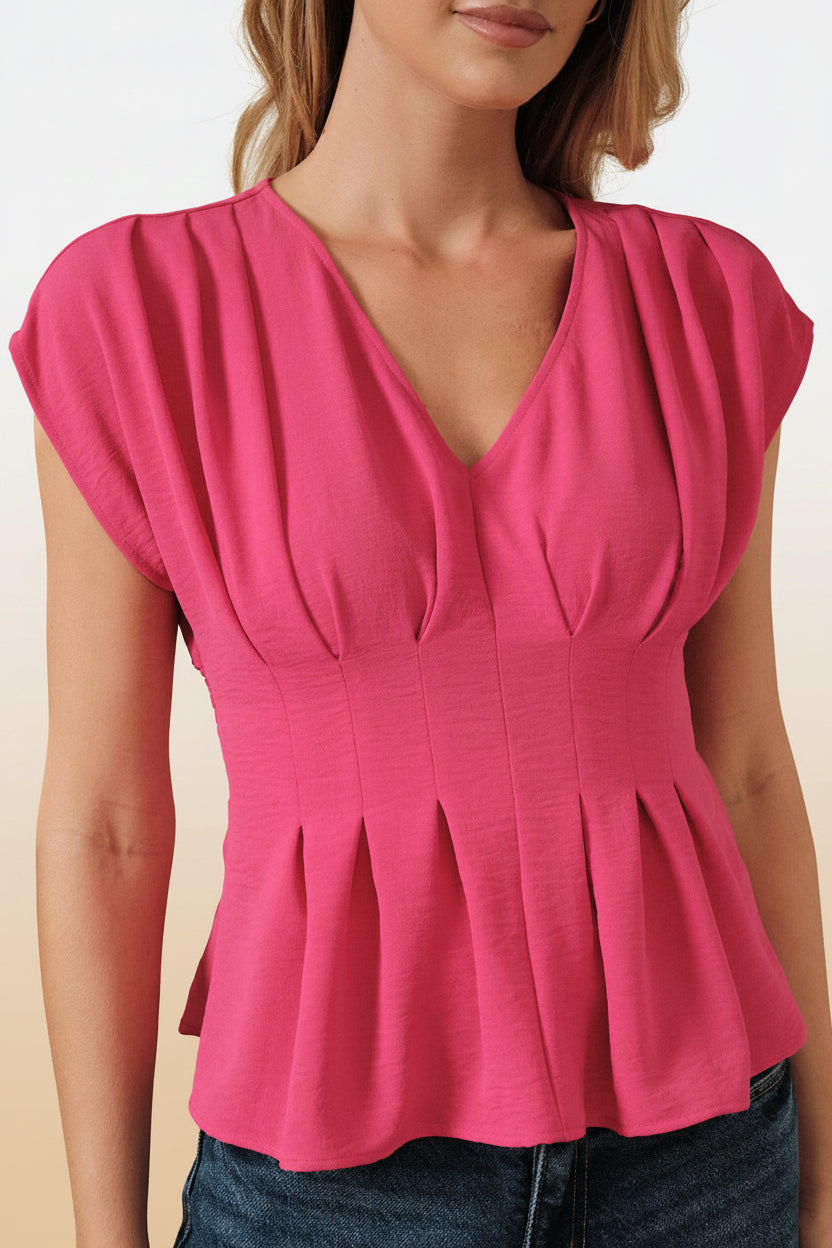Woman wearing a fuchsia pleated peplum top and blue jeans against a beige background