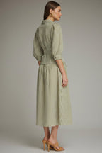 Back view of a woman modeling an olive green and white vertically striped midi dress with three-quarter sleeves and a tie waist and drop waist, paired with tan heeled sandals against a neutral gray studio background.