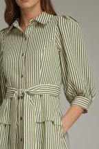 A woman modeling an olive green and white vertically striped midi dress with three-quarter sleeves and a tie waist and drop waist, against a neutral gray studio background.