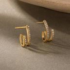 Gold-plated hoop earrings with pave CZ stones on a beige surface