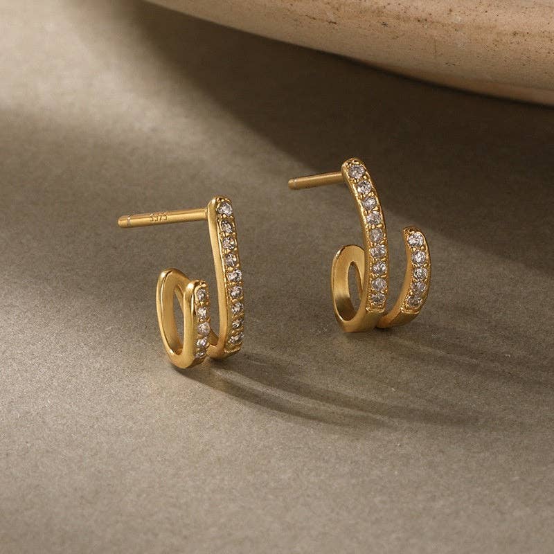 Gold-plated hoop earrings with pave CZ stones on a beige surface