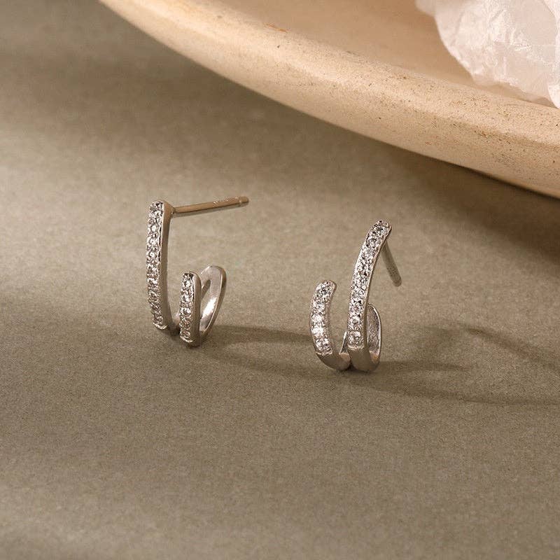 Silver plated hoop earrings with pave CZ stones on a beige surface