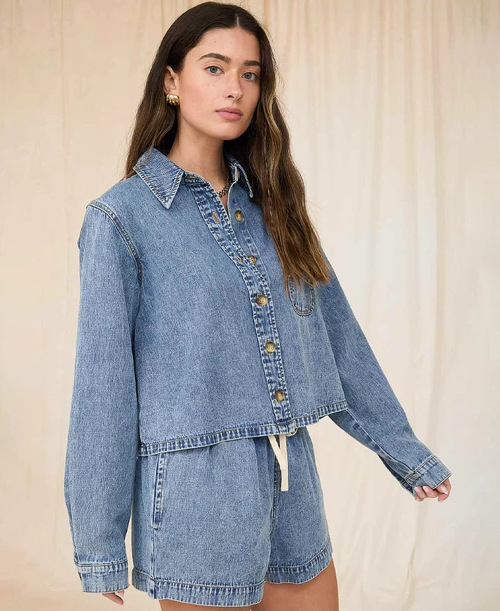 Woman wearing a denim jacket and shorts with a beige top against a neutral background