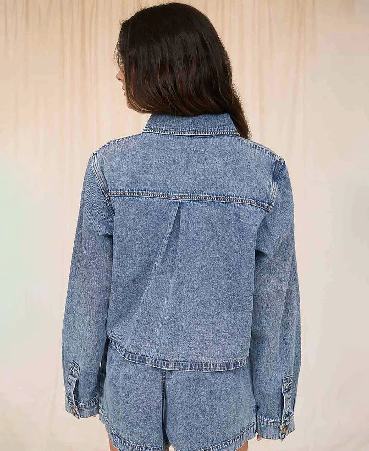 Woman wearing a denim jacket and shorts with a beige top against a neutral background