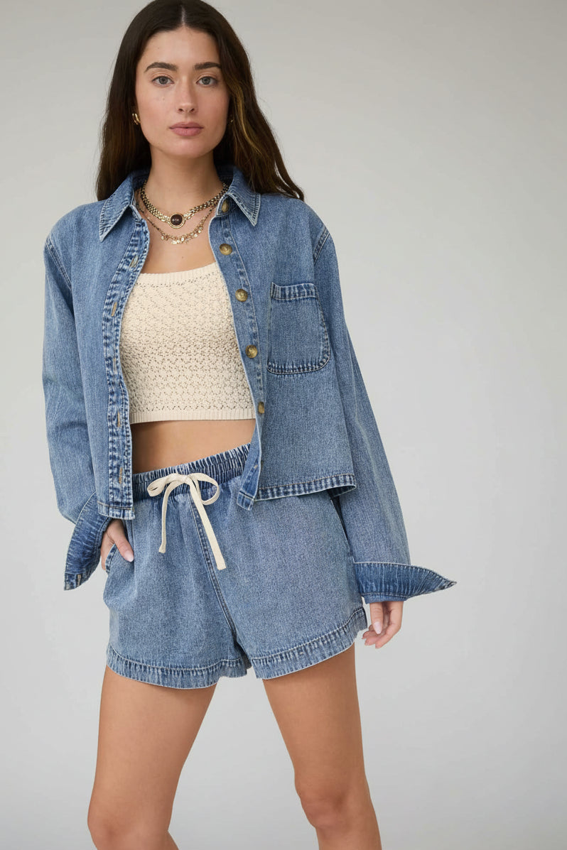 Woman wearing a denim jacket and shorts with a beige top against a neutral background