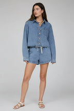 Woman wearing a denim jacket and shorts against a neutral background