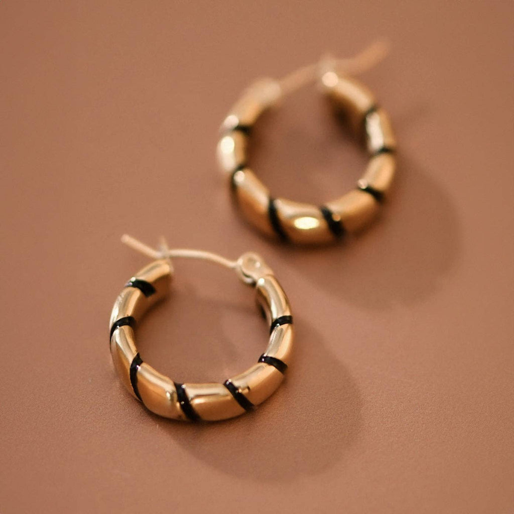 Gold hoop earrings with twisted black enamel  on a brown background