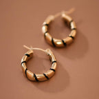 Gold hoop earrings with twisted black enamel  on a brown background