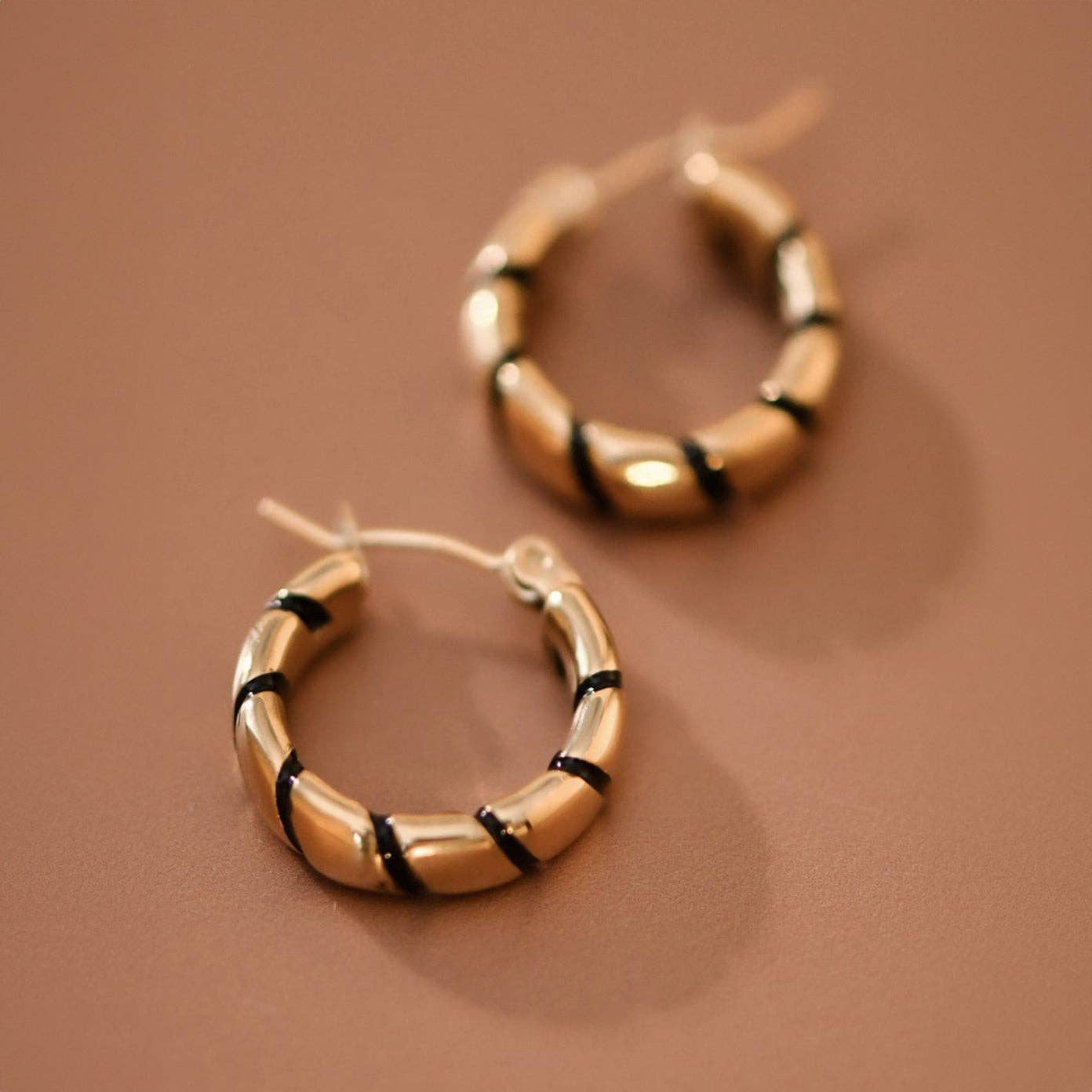 Gold hoop earrings with twisted black enamel  on a brown background