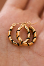 Gold hoop earrings with twisted black enamel on a hand