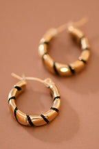 Gold hoop earrings with twisted black enamel on a brown background