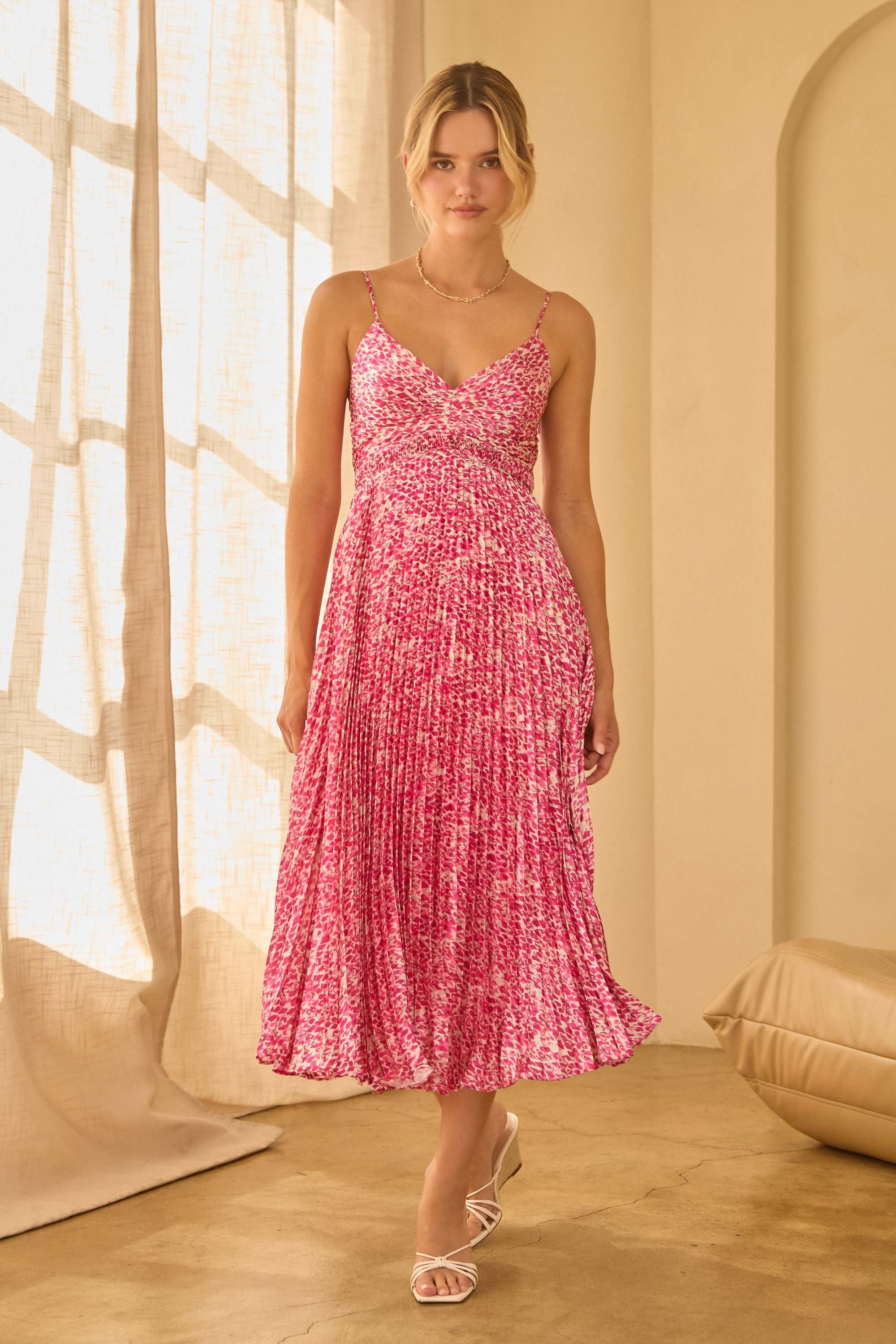 Woman wearing a pink floral spaghetti strap dress with pleated skirt in a softly lit room.