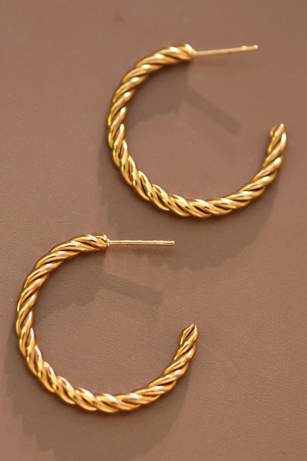 18k gold-plated stainless steel twisted hoop earrings on a brown background