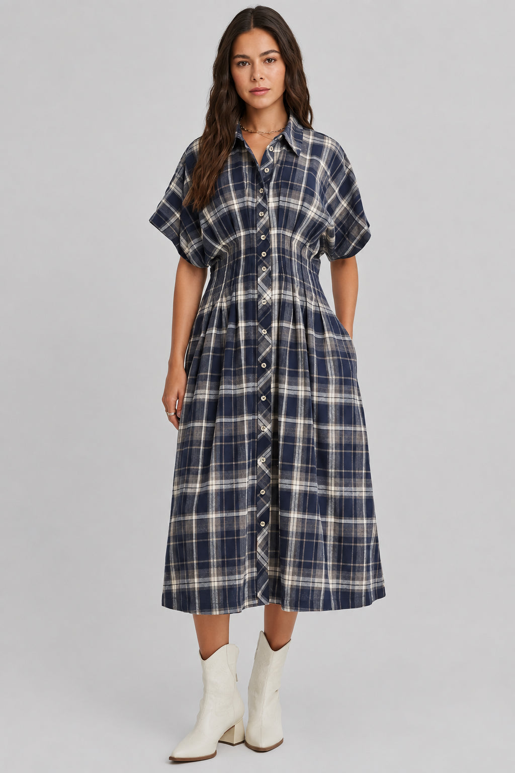 A woman modeling a dolman sleeve button-front midi dress with a navy and cream plaid pattern, paired with white ankle boots, against a plain light beige studio background.