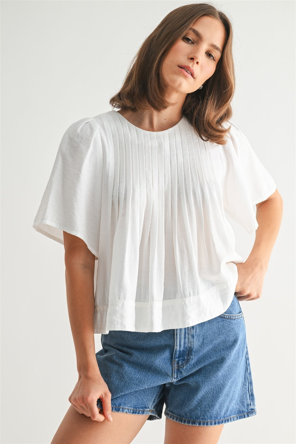 Woman wearing a white pin tuck top and blue jeans against a plain background