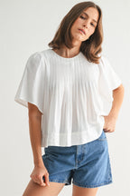 Woman wearing a white pin tuck top and blue jeans against a plain background