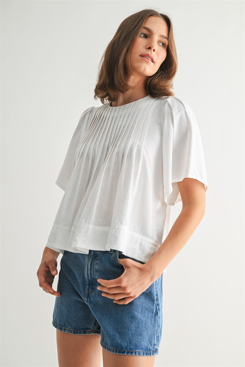 Woman wearing a white pin tuck top and blue jeans against a plain background