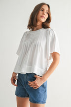 Woman wearing a white pin tuck top and blue jeans against a plain background