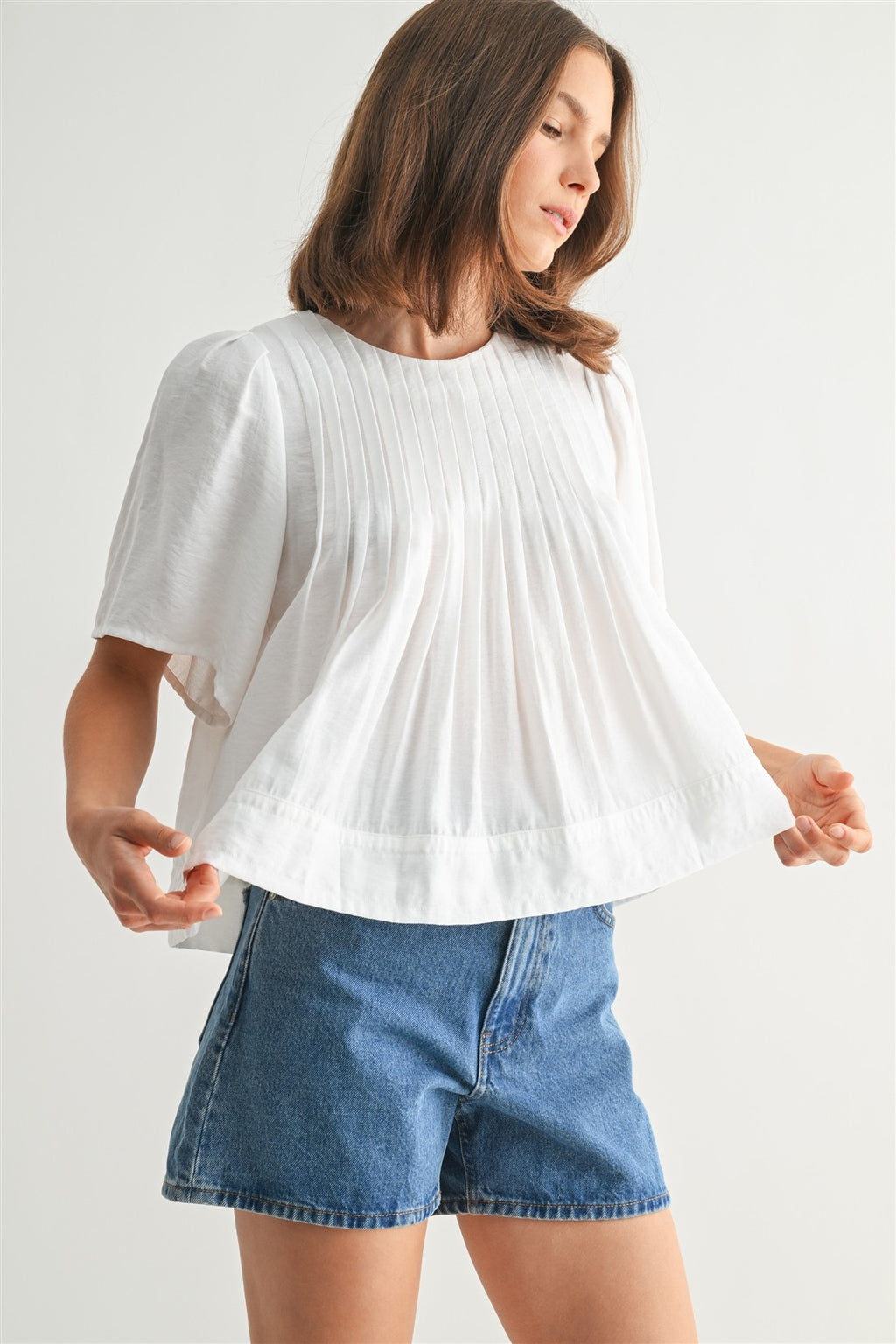 Woman wearing a white pin tuck top and blue jeans against a plain background