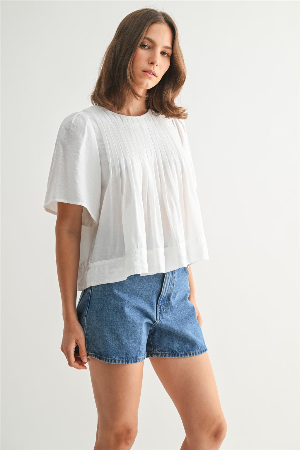Woman wearing a white pin tuck top and blue jeans against a plain background