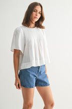 Woman wearing a white pin tuck top and blue jeans against a plain background
