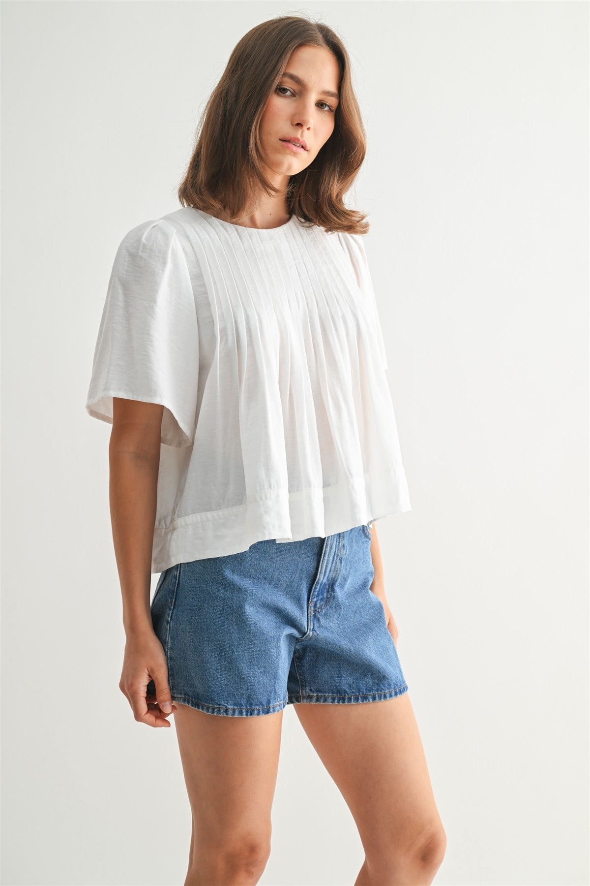 Woman wearing a white pin tuck top and blue jeans against a plain background