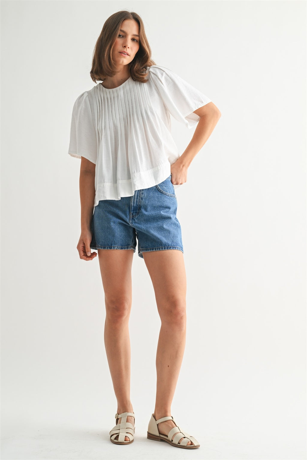 Woman wearing a white pin tuck top and blue jeans against a plain background