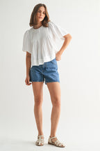 Woman wearing a white pin tuck top and blue jeans against a plain background