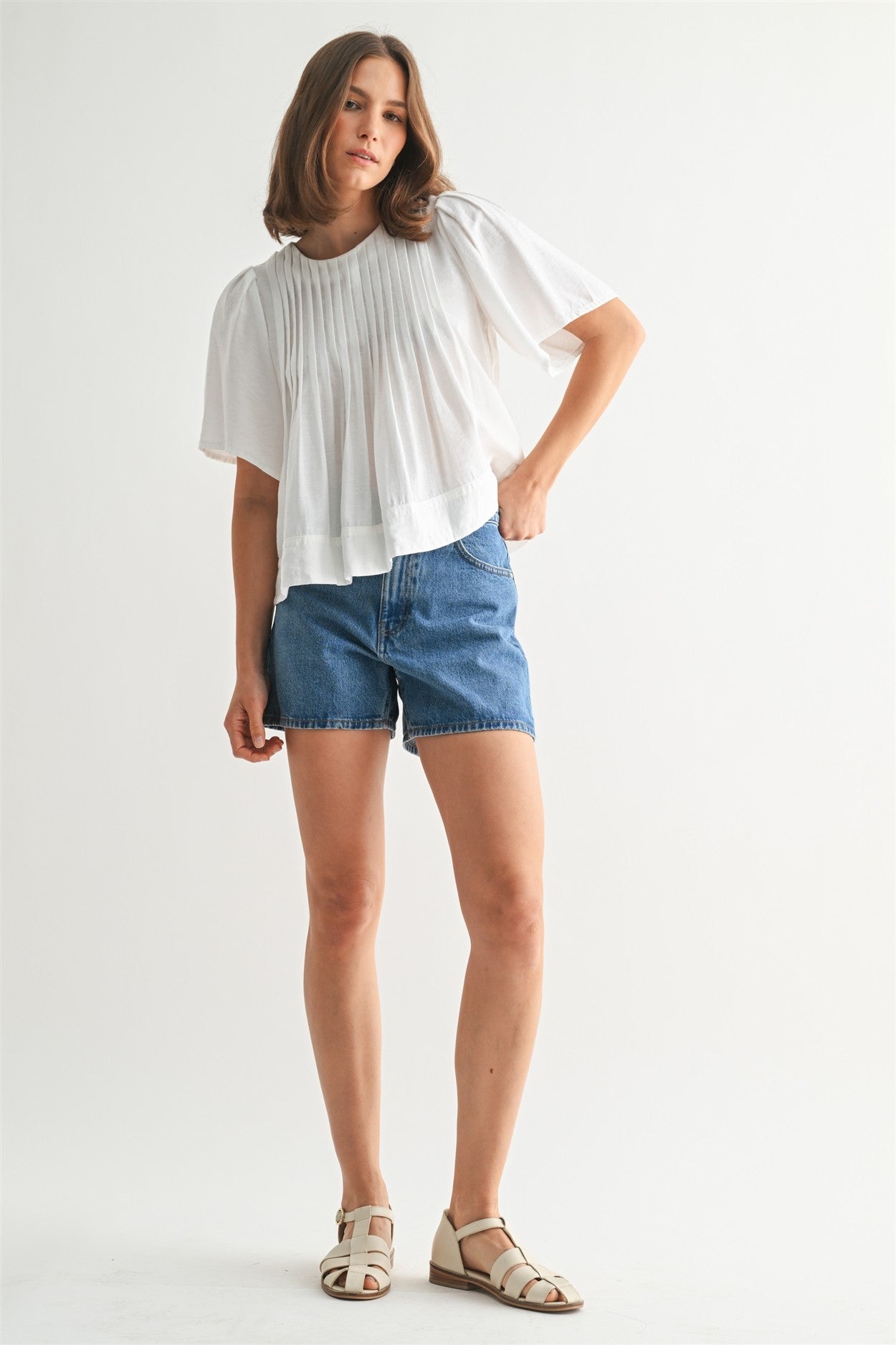 Woman wearing a white pin tuck top and blue jeans against a plain background