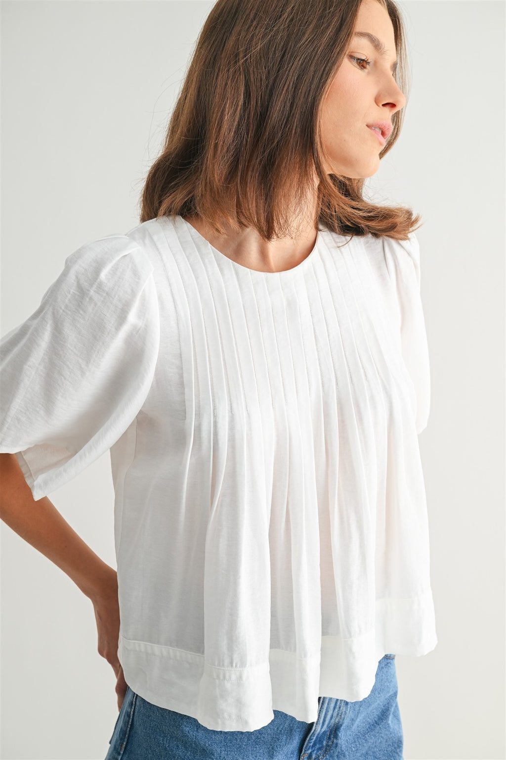 Woman wearing a white pin tuck top and blue jeans against a plain background