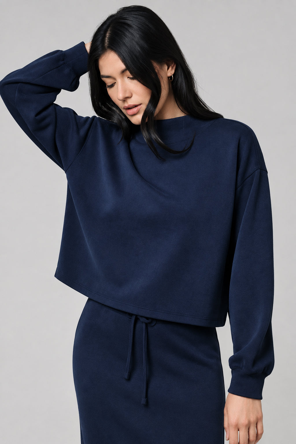 A woman wearing a dark navy blue long-sleeve top and matching drawstring skirt against a neutral beige background.