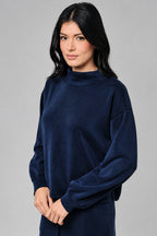 A woman wearing a dark navy blue long-sleeve top and matching drawstring skirt against a neutral beige background.